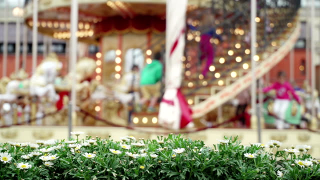 Merry-go-round-carousel.-Happy-children-run-to-carousel-get-best-seats.-Carousel-in-the-background-chrysanthemum-flowers-in-blur