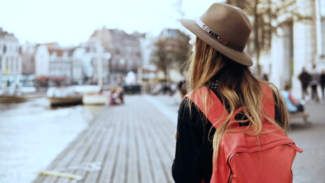 Female-tourist-walks,-takes-photos-on-river-quay.-Girl-with-long-hair,-red-backpack-sends-pictures-to-friends-online.-4K