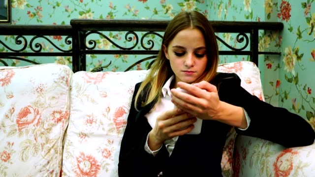 Young-business-woman-in-suit-uses-smartphone-on-the-sofa