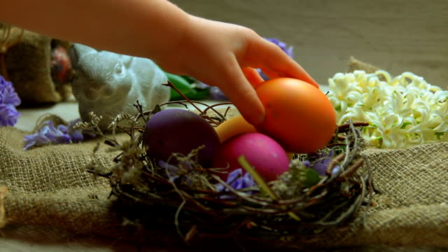 Child's-hand-lays-colored-egg-in-in-the-Easter-nest