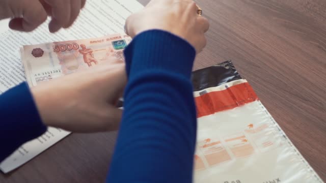 Woman-hands-puts-pile-of-ruble-banknotes-money-into-plastic-envelope