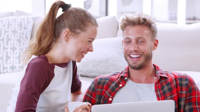 Joven-pareja-blanca-sentada-en-el-suelo-en-casa-utilizando-la-computadora-portátil