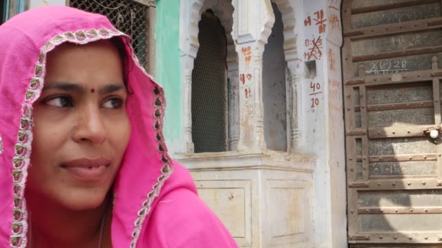 Pan-close-up-from-a-handsome-man-with-red-turban-to-a-pretty-lady-in-pink-sari-talking-in-front-of-a-decorative-entry-old-haveli-building