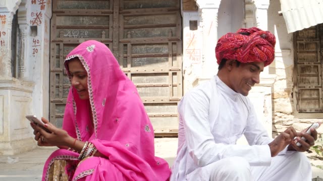 Pan-down-to-a-couple-in-Rajasthani-traditional-dress-busy-ignoring-on-their-own-cell-phones,-hectic-separate-lifestyle