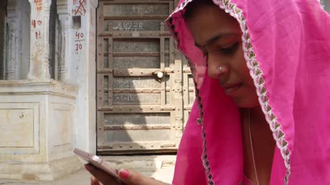 Neigung-bis-zu-einer-indischen-Ethnizität-Frau-in-Rosa-Saree-beschäftigt-auf-ihrem-Smart-phone-beobachten-Chat-video-Internet
