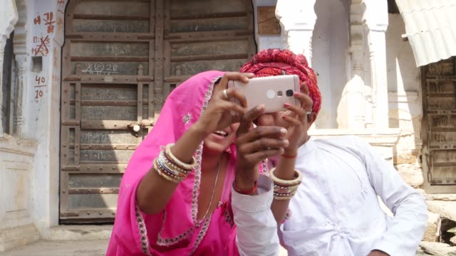 Tilt-down-to-a-traditional-couple-taking-camera-selfie-on-mobile-phone-photography-in-Rajasthan-India
