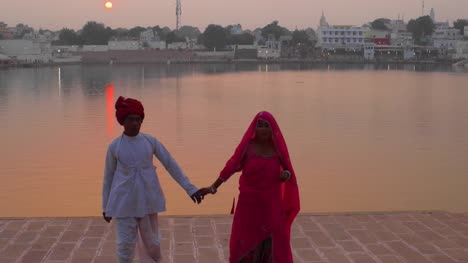 Romantischen-indischen-Ehepaar-in-Tracht-zu-Fuß-entfernt-von-einem-Sonnenuntergang-am-See
