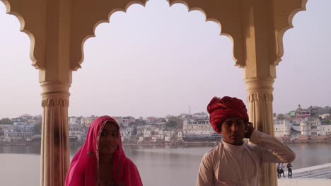 Tilt-down-to-attractive-Indian-couple-in-traditional-dress-with-Pushkar-lake-in-the-background,-Rajasthan,-India