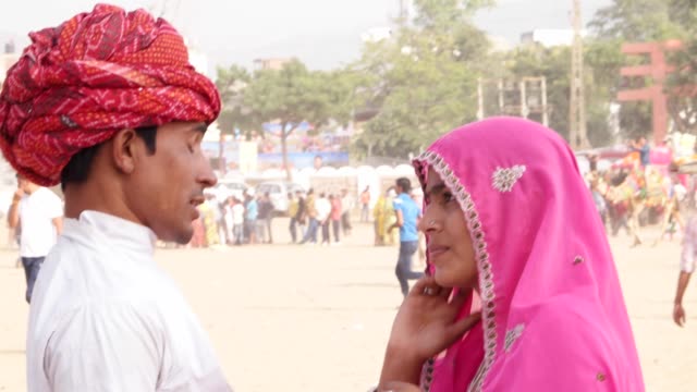 Pan-left-to-Rajasthani-smart-and-beautiful-couple-at-the-busy-fairgrounds-of-Pushkar-Fair,-India