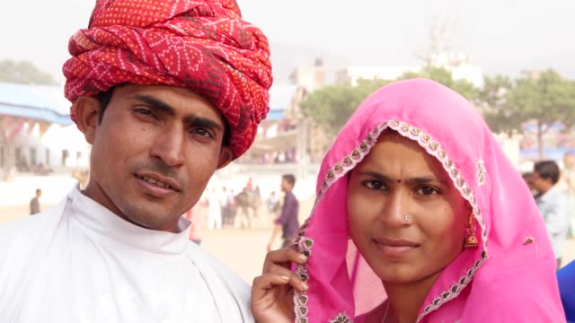 Tilt-up-to-attractive-Indian-couple-looking-straight-to-the-camera-at-the-fairgrounds-of-Pushkar-Fair,-Rajasthan,--India