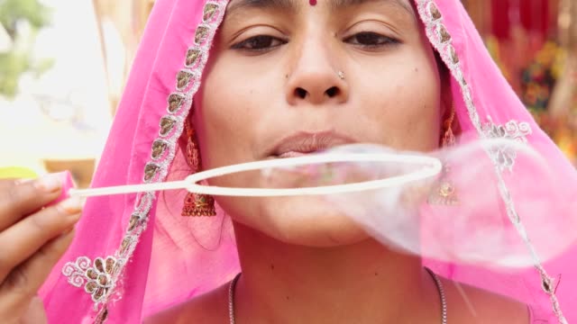 Wife-in-pink-sari-blows-bubbles-while-her-husband-in-black-sunglasses-and-red-turban-watches