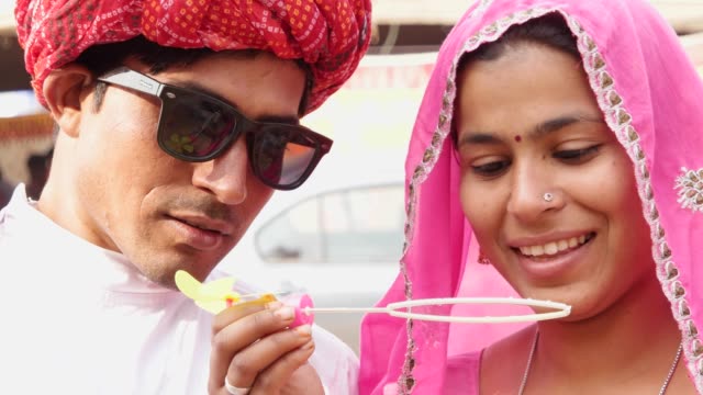 Attraktives-Rajasthani-paar-Spaß-bläst-Seifenblasen-und-tragen-ethnischen-traditionelle-indische-Kleidung-bei-Pushkar-Camel-fair,-Indien