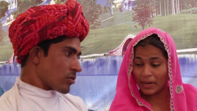 Paar-sprechen-sitzen-vor-einem-gemalten-Zelt-auf-der-Pushkar-Mela-Festival-Camel-Fair,-Rajasthan,-Indien