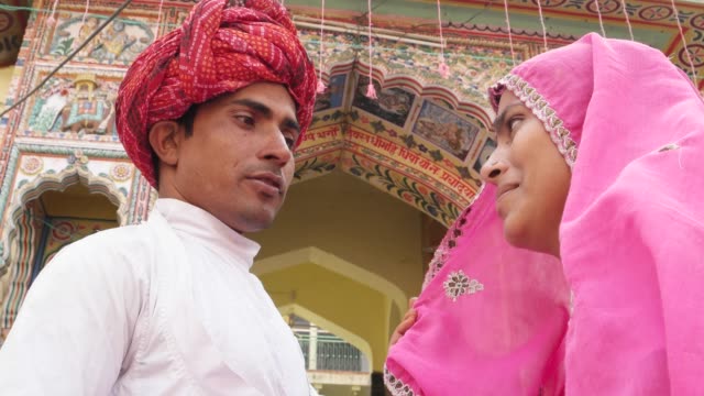Hermosa-mujer-en-sari-rosa-y-atractivo-hombre-de-turbante-rojo-fuera-de-un-templo-de-Pushkar,-Rajasthan,-India