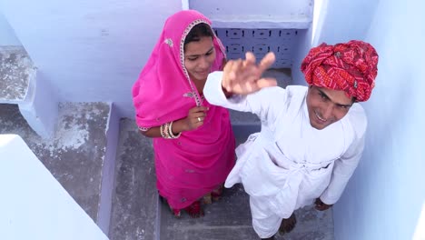 handheld-overhead-shot-of-Beautiful-bride-and-groom-waving-goodbye-from-a-staircase,-posing,-dolly-in-in-Pushkar,-Rajasthan,-India