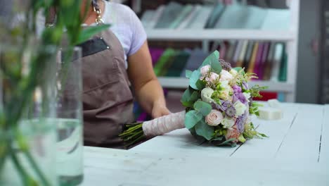 professional-florist-arranging-with-ribbon-flower-wedding-bouquet-in-floral-design-studio