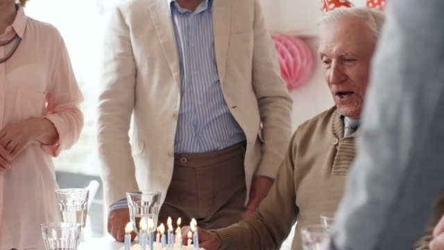 Elderly-Man-Blowing-Off-Candles-at-Birthday-Dinner-Party