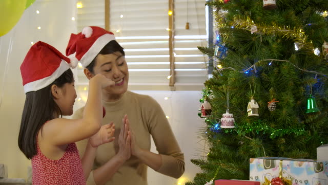 Mother-and-daughter-decorating-Christmas-tree,-Young-girl-putting-ornament-on-Christmas-tree-in-slow-motion