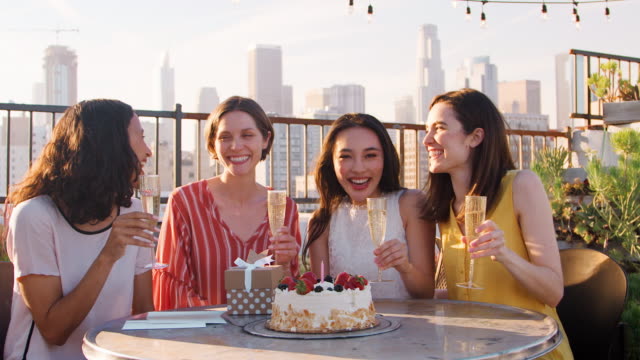 Porträt-von-Freundinnen-Geburtstag-auf-Dachterrasse-mit-Skyline-der-Stadt-im-Hintergrund