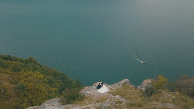 Young-and-beautiful-wedding-couple-together-on-the-slope-of-the-mountain-near-sea.-Lovely-groom-and-bride.-Shooting-from-the-air.-Aerial-shot