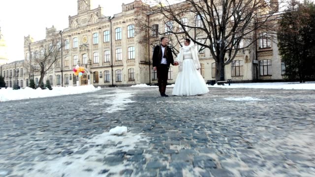 Winter-Hochzeit.-Brautpaar-in-Brautkleider-sind-Fuß-durch-den-tief-verschneiten-Park,-vor-dem-Hintergrund-der-antiken-Architektur-und-Pflastersteine