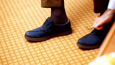 close-up,-men's-hands-tie-shoelaces.-man-is-putting-on-his-stylish-blue-suede-shoes,-on-carpet-background.-Groom-preparing-for-the-wedding