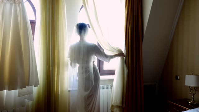 a-bride,-beautiful-girl,-in-veil-and-white-peignoir,-robe,-looks-out-the-window.-Morning-of-the-bride