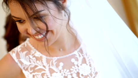 close-up,-bride-fees.-the-bride-is-dressed-for-the-wedding.-portrait-of-a-beautiful,-smiling-bride,-in-veil-and-lace-dress.-Bridesmaid-laces-up-white-lace-dress-with-ribbon.-Wedding-dress-details