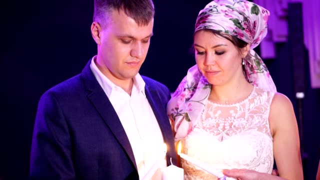 wedding-traditions,-ceremonies.-the-newlyweds-are-holding-a-white-large-candle-symbol-of-the-family-hearth,-happiness-and-well-being.-parents-light-a-candle-of-the-newlyweds-with-their-candles