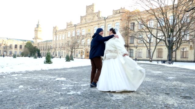 winter-wedding.-newlywed-couple-in-wedding-dresses-are-dancing-wedding-dance-in-a-snow-covered-park,-against-the-background-of-ancient-architecture-and-paving-stones