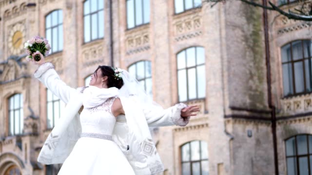 Porträt-einer-schönen-Braut,-in-einem-weißen-Kleid,-Schleier-und-Pelz-Mantel.-Braut-ist-Spinnerei,-und-glücklich-lächelnd,-hält-einen-Brautstrauß.-vor-dem-Hintergrund-der-antiken-Architektur-winter-Hochzeit