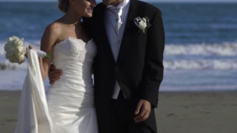 Sonriente-pareja-de-recién-casados-caminando-por-la-playa