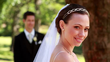 Braut-lächelnd-in-die-Kamera-mit-Bräutigam-stehen-im-Hintergrund