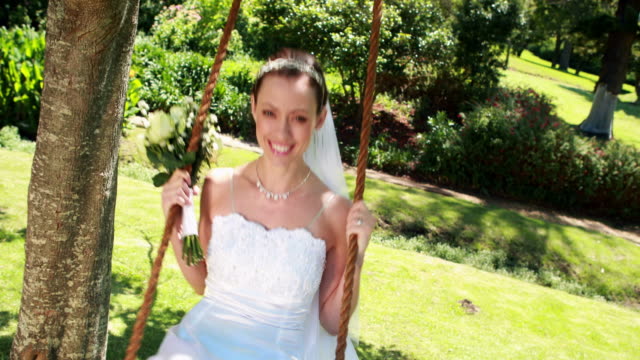 Smiling-bride-sitting-on-a-swing-looking-at-camera