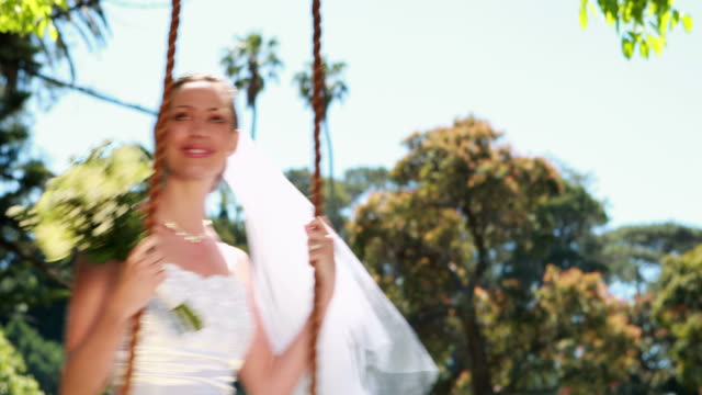 Pretty-bride-sitting-on-a-swing-smiling-at-camera