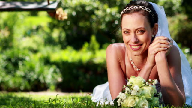 Wunderschöne-Braut-lächelnd-in-die-Kamera-liegen-auf-dem-Rasen