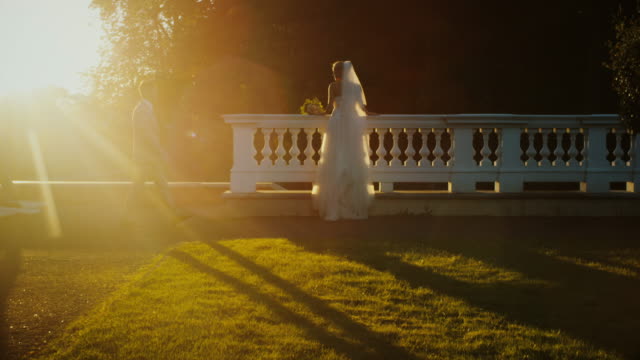 Braut-und-Bräutigam-schauen-sich-den-Sonnenuntergang-von-einem-Balkon-in-einem-Park-aus-an.