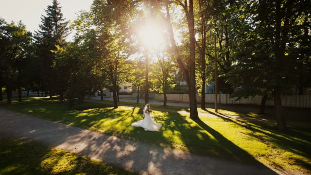 Aerial-drone-shot-of-a-happy-bride-in-a-wedding-dress-walking-in-a-park.