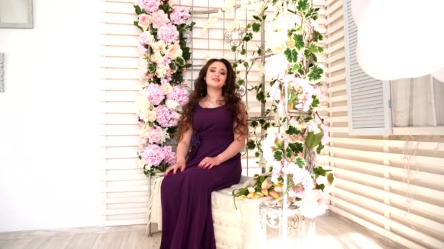 Young-woman-in-purple-dress-sits-on-wedding-bench-with-flowers