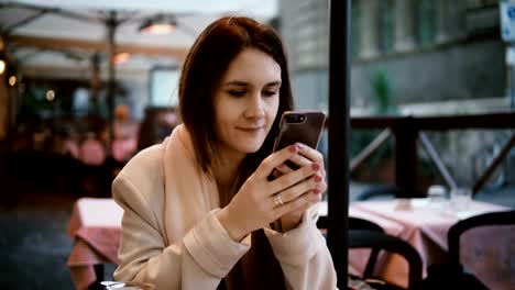 Young-beautiful-woman-sitting-in-cafe-in-evening-and-using-the-smartphone.-Beautiful-female-surfing-the-Internet