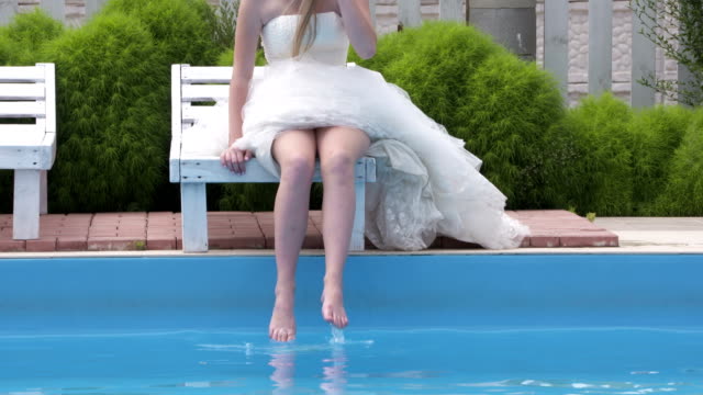 Young-barefoot-girl-in-white-wedding-dress-beside-swimming-pool