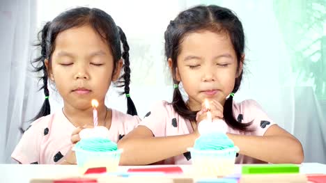 Zwei-asiatische-Zwillingsmädchen-vornehmen-gefaltete-Hand-wollen-die-guten-Dinge-für-ihren-Geburtstag.-Dolly-im-Studio-gedreht.