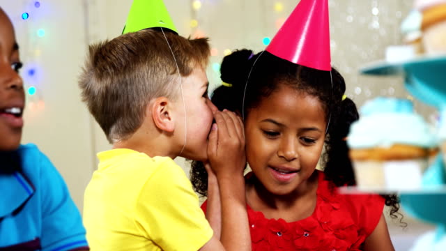 Boy-whispering-to-girl-while-sitting-with-friends-during-birthday-party-4k