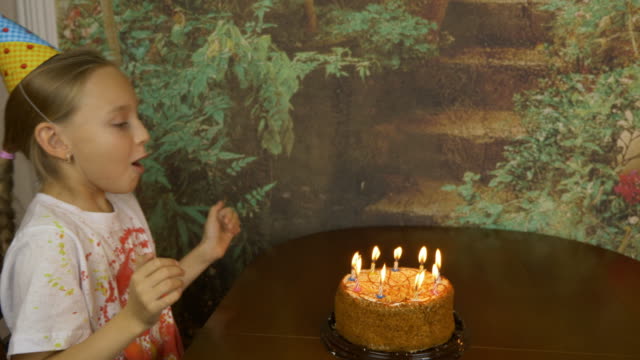 Funny-girl-can-not-blow-birthday-candles-on-cake.-Joke-party-at-home.-Young-girl-blowing-candles-on-cake.-Lot-of-smoke-and-ash-on-table.-Fast-motion-effect.-Girl-clapping.