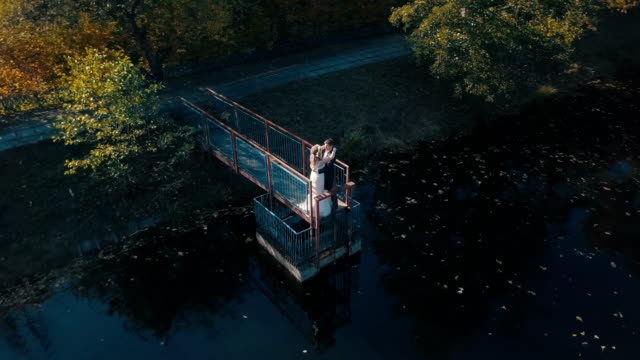 Junge-Brautpaar-steht-auf-einer-kleinen-Brücke-in-der-Nähe-von-schönen-See
