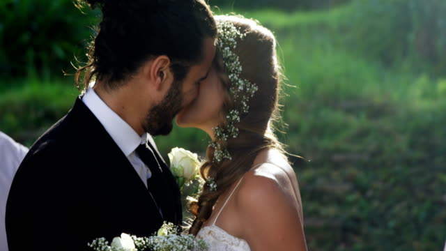 Braut-und-Bräutigam-küssen-und-im-Hintergrund-Gäste-werfen-Blütenblätter-4K-4k