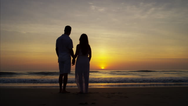 Silueta-de-joven-pareja-española-disfrutando-de-sunrise-beach
