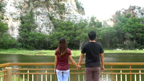 Man-and-woman-or-couple-walk-together-holding-hands-in-nature-with-mountain-and-river.-Happy-freedom-and-travel-concept.