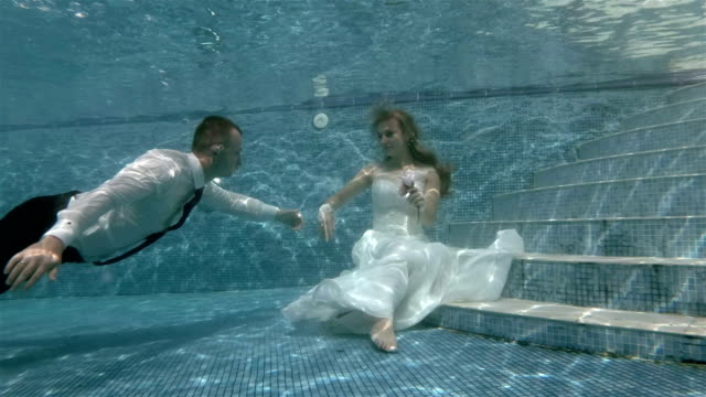 4K-schwimmt-unter-Wasser-der-Bräutigam-der-Braut,-die-sitzt-auf-dem-Boden-des-Beckens-und-küsst-ihre-hand