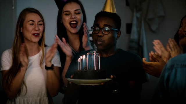 African-American-guy-makes-wish,-blows-on-candles.-Happy-multi-ethnic-friends-share-birthday-party-celebration.-4K